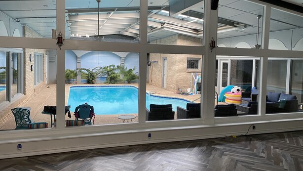 A room with a large window overlooking a swimming pool, equipped with outdoor furniture and a ceiling fan. - Our Pool House (Lubbock)
