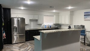 A modern kitchen with white cabinets, a stainless steel refrigerator, a granite countertop, and a herringbone-patterned floor. - Our Pool House (Lubbock)