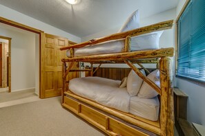 A bunk bed with a wooden frame and white bedding in a room with a wooden door and window blinds.