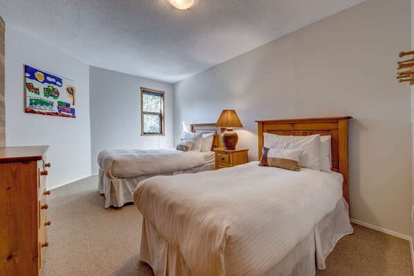 A bedroom with two beds, a wooden dresser, a lamp, and a window.