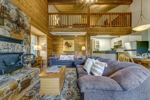 A cozy living room with a stone fireplace, a sofa set, and a dining area with a kitchen in the background. - Telemark 8 - Ski in Walk out, Private Sauna, Short Walk to the Village (Whistler)