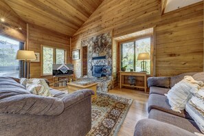 A cozy cabin interior with wooden walls, a stone fireplace, a television, and a comfortable seating area.