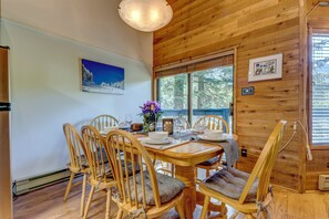 A wooden-paneled dining room with a table set for four, chairs with cushions, a vase of flowers, and a painting on the wall.