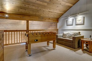 Une pièce chaleureuse avec un plafond en bois, une table de baby-foot, un canapé et deux tableaux encadrés au mur.