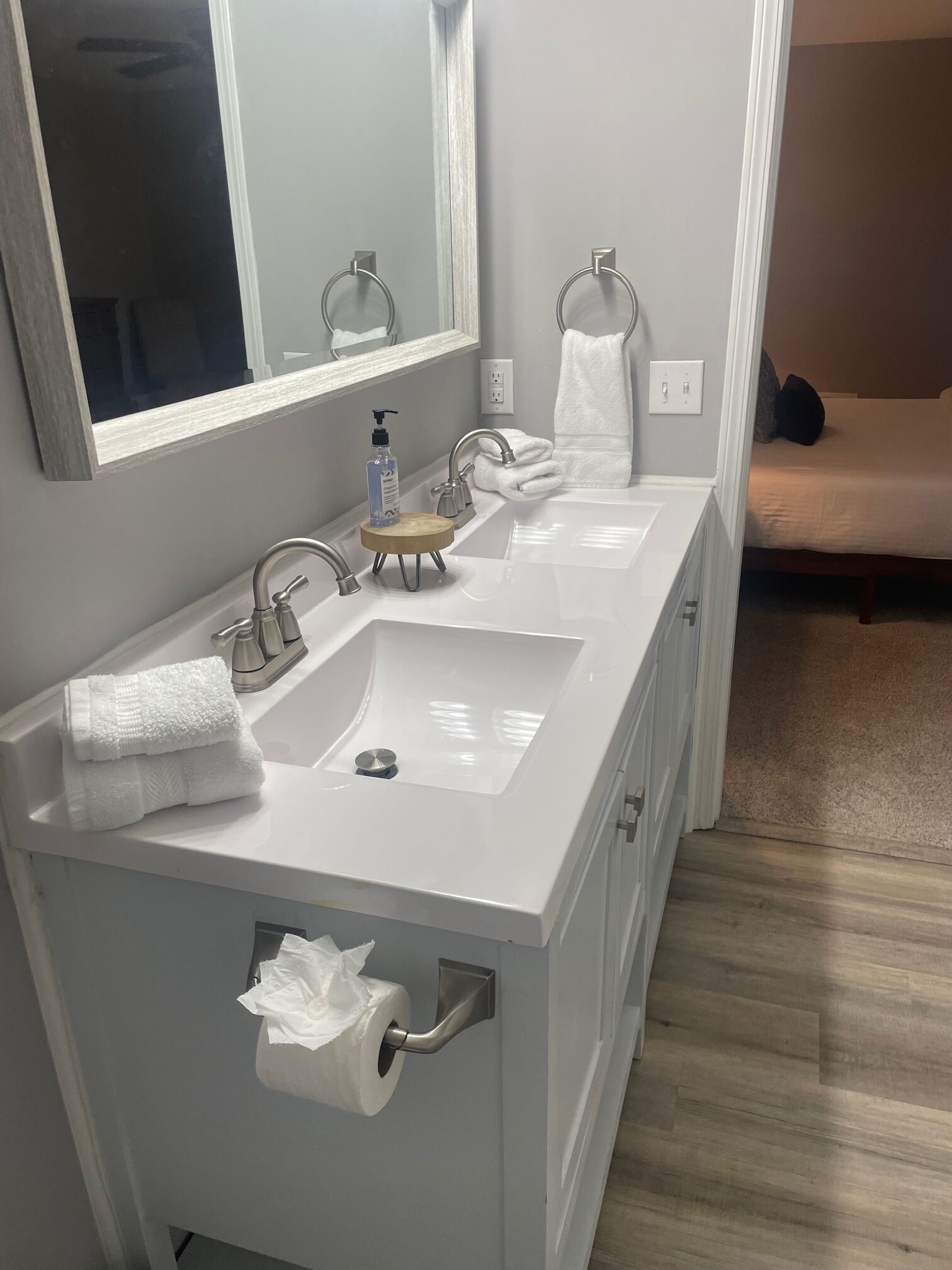 A bathroom with a double sink, a mirror, a towel rack, and a toilet paper holder.