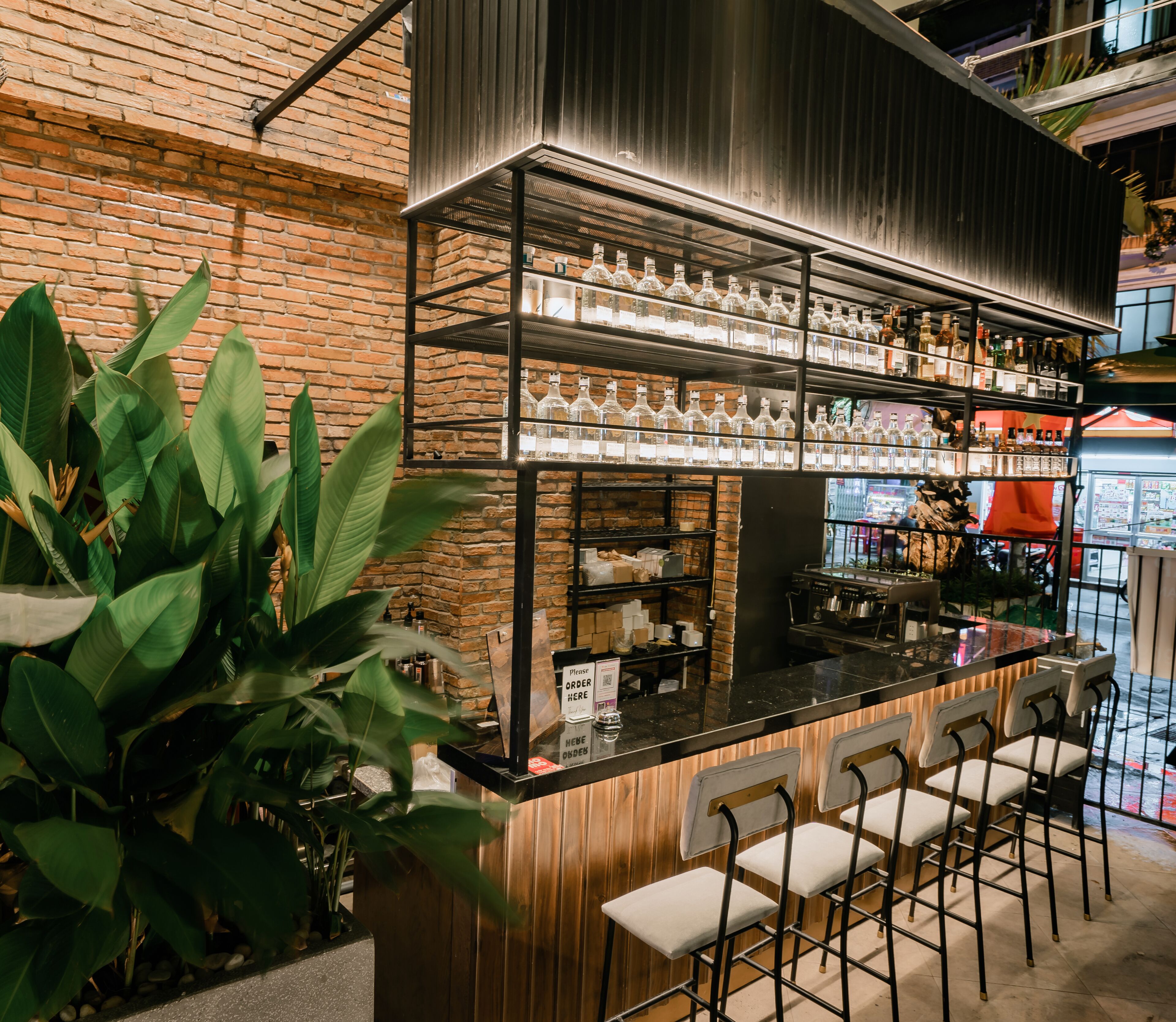 Uma área de bar com parede de tijolos, prateleiras cheias de garrafas e banquetas.