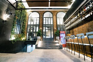 A modern interior with a brick wall, arched windows, a staircase, and a bar area with shelves. - MINT HOTEL (Ho Chi Minh City)