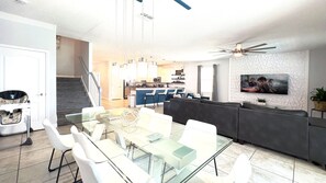 A modern living room with a glass dining table, a gray sofa, and a kitchen in the background.