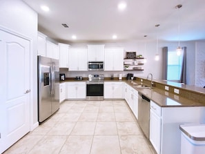 A modern kitchen with white cabinets, stainless steel appliances, and a granite countertop. - Endless Oasis | Pool, Spa, Game Room near Disney (Davenport)