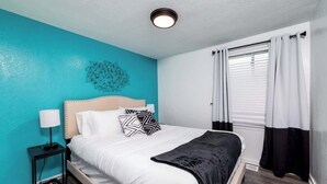 A bedroom with a bed, a nightstand, a wall art piece, and a window with curtains. - Little Lansing House I 3 BR w/ Queen beds (Lansing)