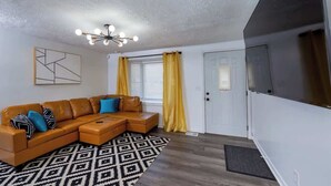 A living room with a sectional sofa, a patterned rug, a ceiling light fixture, and a door with a window. - Little Lansing House I 3 BR w/ Queen beds (Lansing)