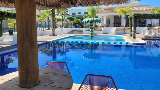 Una piscina con techo de paja, rodeada de sillas de descanso blancas y palmeras.