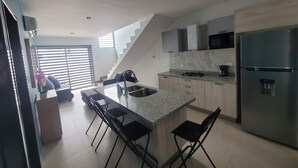 Una cocina moderna con una isla central, taburetes de bar, un refrigerador de acero inoxidable y un microondas.