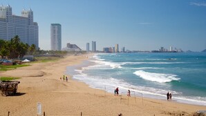 Una playa con una red de voleibol, palmeras y un horizonte urbano al fondo.
