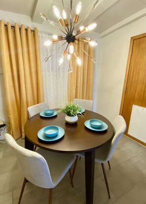 Zona pranzo con tavolo rotondo, quattro sedie, una pianta in vaso e un lampadario moderno.