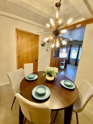 A dining area with a round table, four chairs, a wooden door, and a ceiling light fixture.