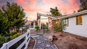 Una casa moderna con fachada de piedra, exterior blanco y camino de entrada pavimentado que conduce a una cerca blanca.