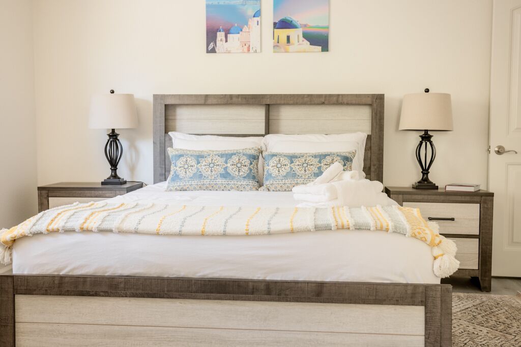 A bed with a wooden headboard, two bedside tables with lamps, and a wall with two framed pictures.