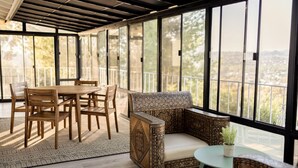 Un patio techado con una mesa y sillas de madera, un sofá estampado y una mesita con una planta.