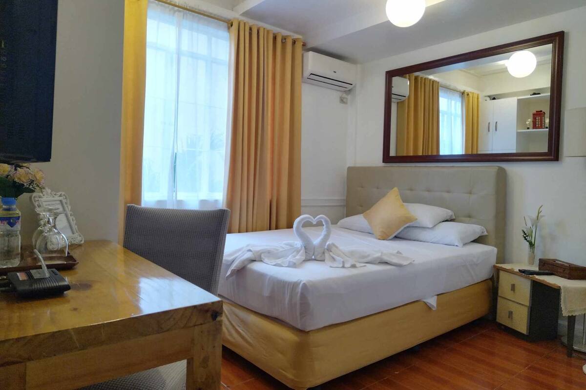 A hotel room with a bed, bedside table, chair, and a desk with a mirror.