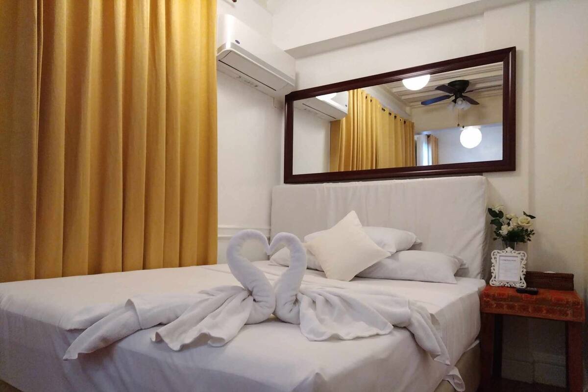 A hotel room with a neatly made bed, a mirror above the bed, and a small table with a vase of flowers.