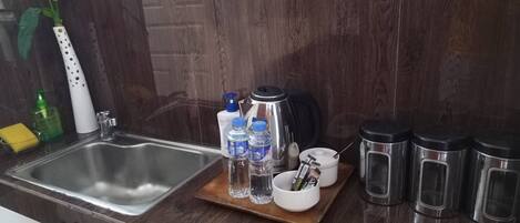 Una cocina con un lavamanos de acero inoxidable, una bandeja de madera con botellas y una cafetera, y recipientes negros para condimentos.