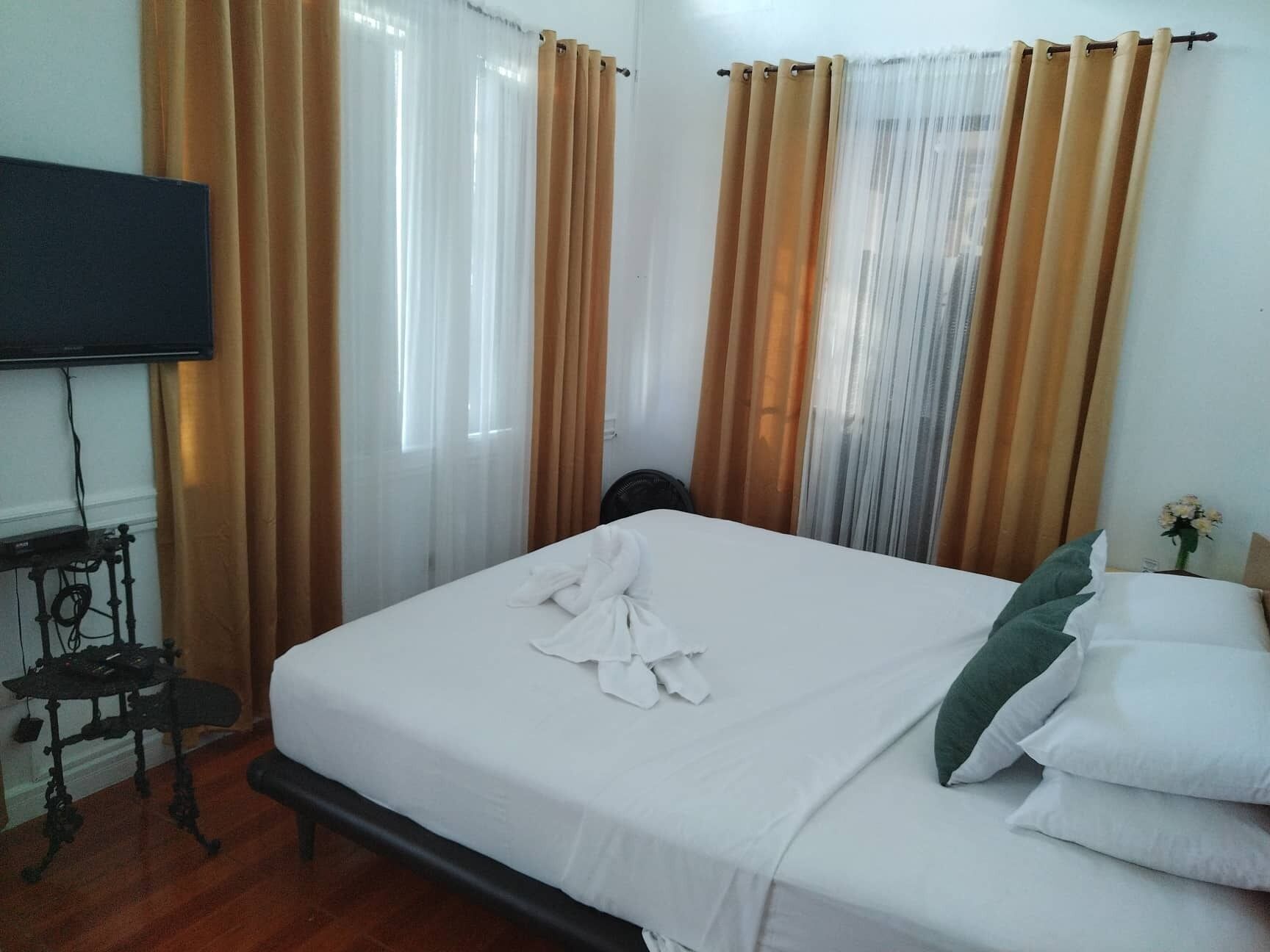 Ein Hotelzimmer mit einem Bett, Vorhängen, einem Fernseher und einem kleinen Tisch.