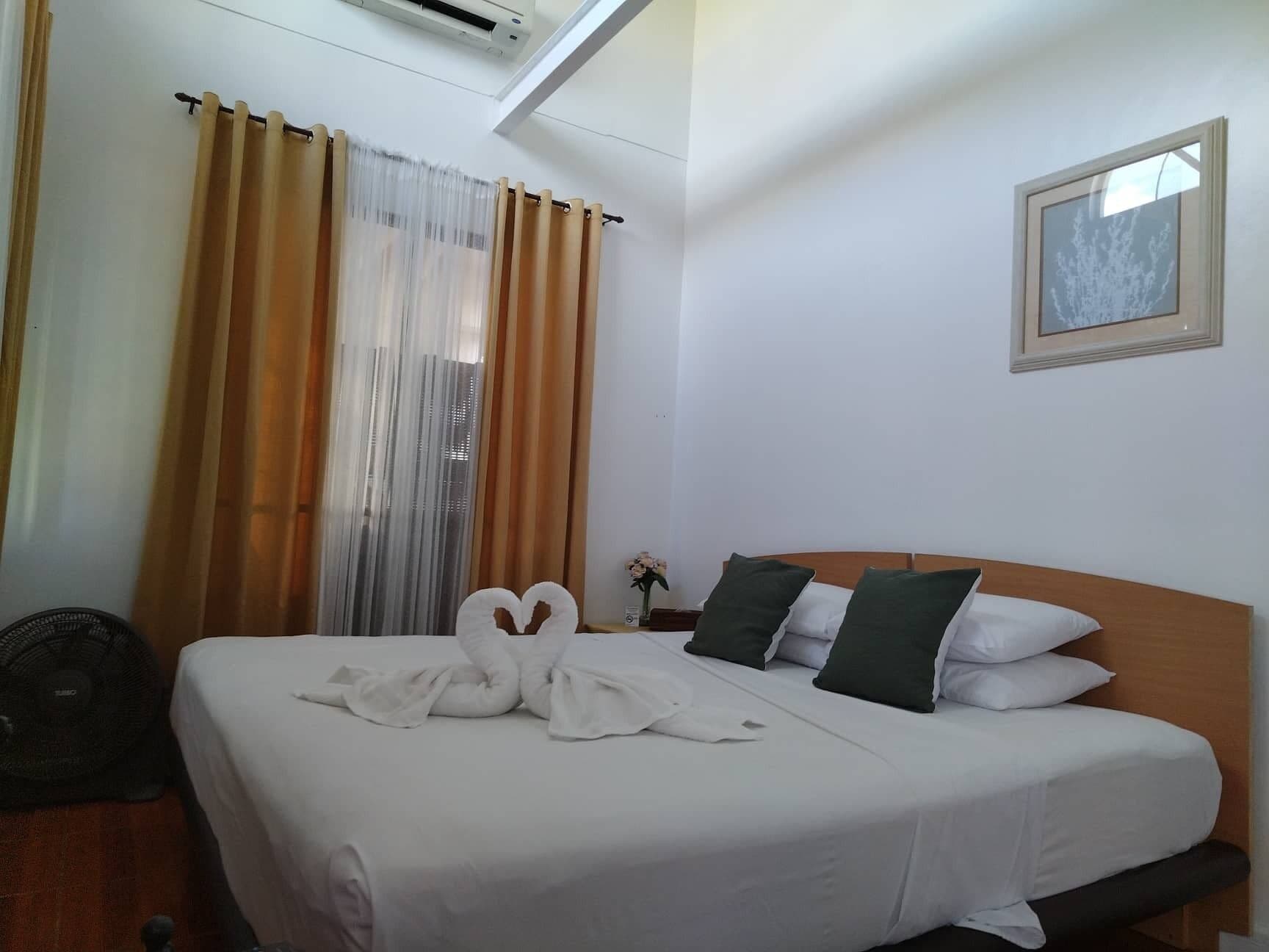 Ein Hotelzimmer mit einem ordentlich bezogenen Bett, einem Ventilator und einem Fenster mit Vorhängen.