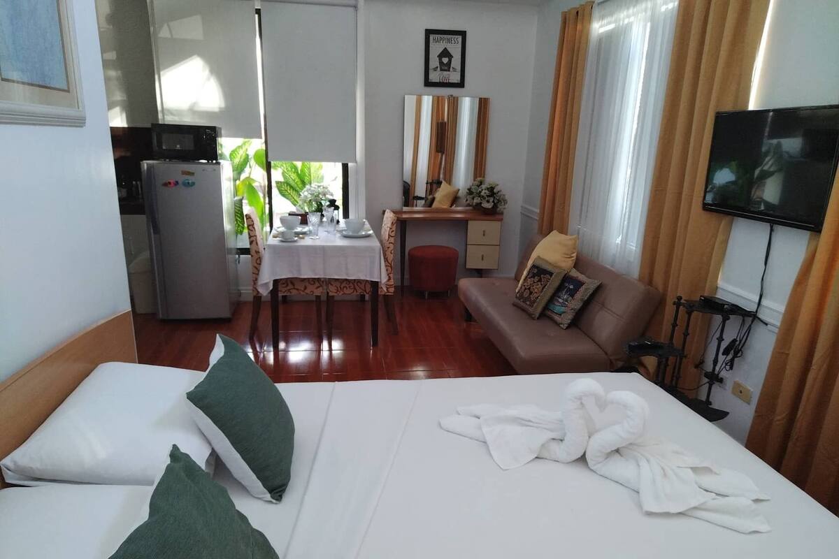 A hotel room with a bed, a desk, a sofa, a TV, and a dining area.