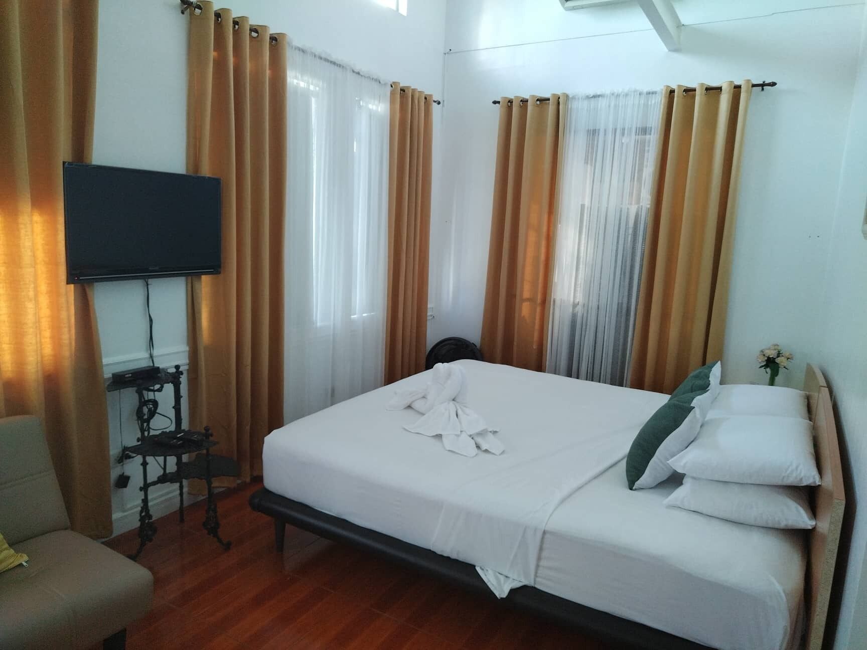 A hotel room with a bed, curtains, a TV, and a desk with a chair.
