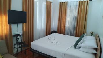 A hotel room with a bed, curtains, a TV, and a desk with a chair.