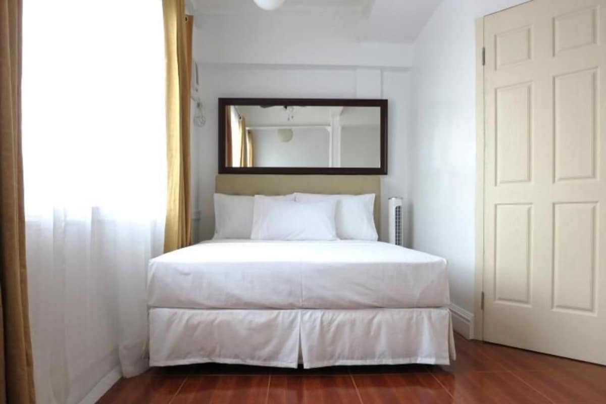 A bedroom with a bed, a mirror, a door, and a window with curtains.