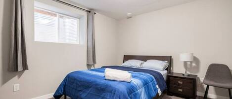 A bedroom with a bed, a nightstand, a lamp, and a chair.