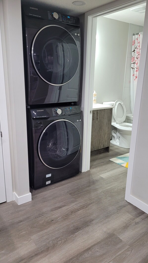 A laundry room with two black Samsung washing machines. - Luxury 2 Bedroom Suite (Airdrie)