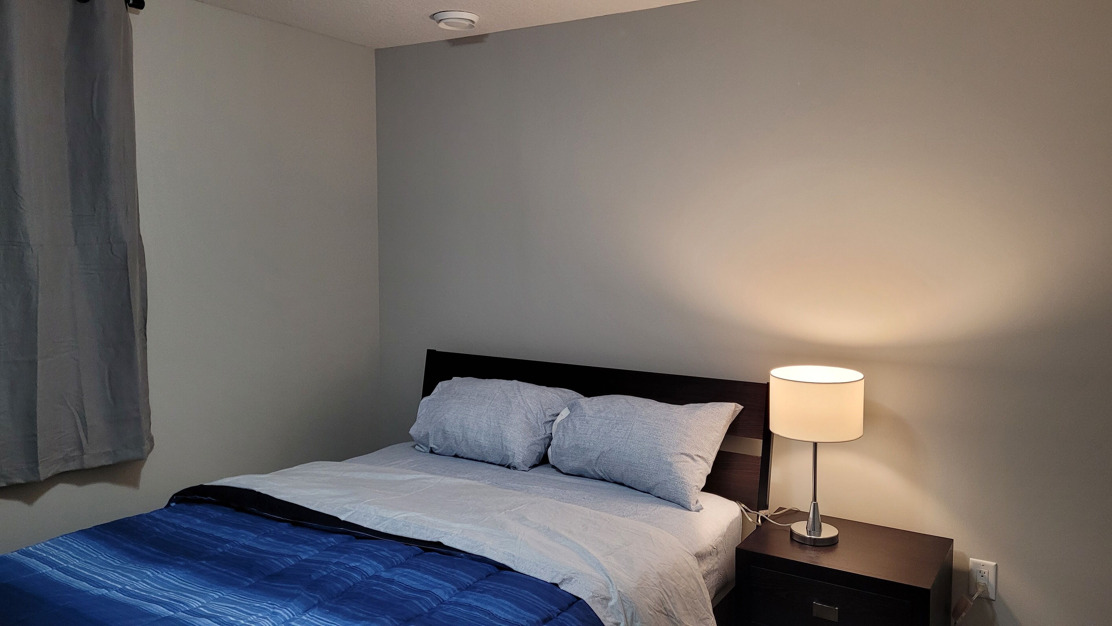 A neatly made bed with a blue blanket, a bedside lamp, and a dark wooden nightstand.