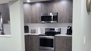 A modern kitchen with grey cabinetry, a stainless steel microwave, a built-in oven, and a coffee maker. - Luxury 2 Bedroom Suite (Airdrie)