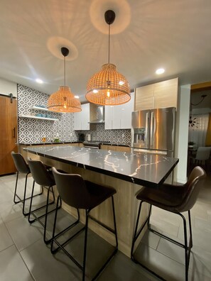 A modern kitchen with a central island, black bar stools, and pendant lighting.