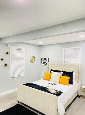 Un dormitorio con cama, paredes blancas y ventana con persianas.