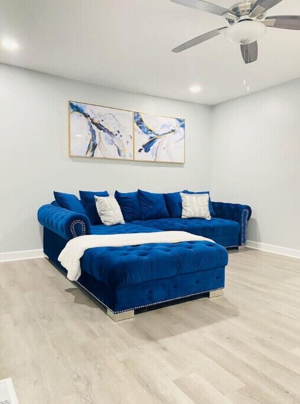 Un dormitorio con un sofá cama grande de color azul, un ventilador de techo y arte abstracto en la pared.