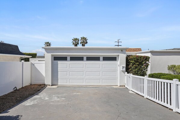 Un garage avec une porte blanche, une clôture blanche et un petit arbre sur le toit.