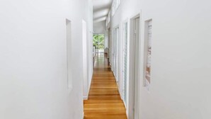 Un couloir étroit, doté d’un plancher en bois et de murs blancs, mène à une pièce avec une grande fenêtre.