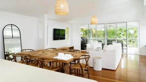 Un espace de repas moderne avec une table et des chaises en bois, un canapé blanc et de grandes fenêtres donnant sur un paysage verdoyant.
