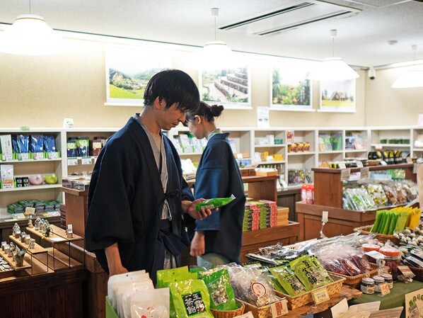 Interior de una tienda con estantes llenos de productos envasados, una caja registradora y una exhibición de frutas y verduras frescas.