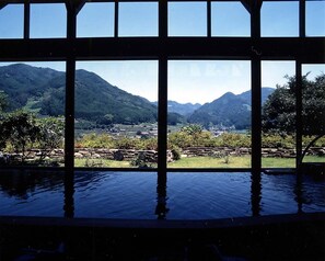 Vista a través de una ventana con una piscina al frente, paisaje montañoso y cielo despejado.
