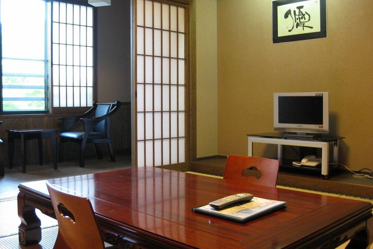 Une pièce de style japonais traditionnel, avec un sol recouvert de tatamis, une table en bois, des chaises, un téléviseur et une porte coulissante.