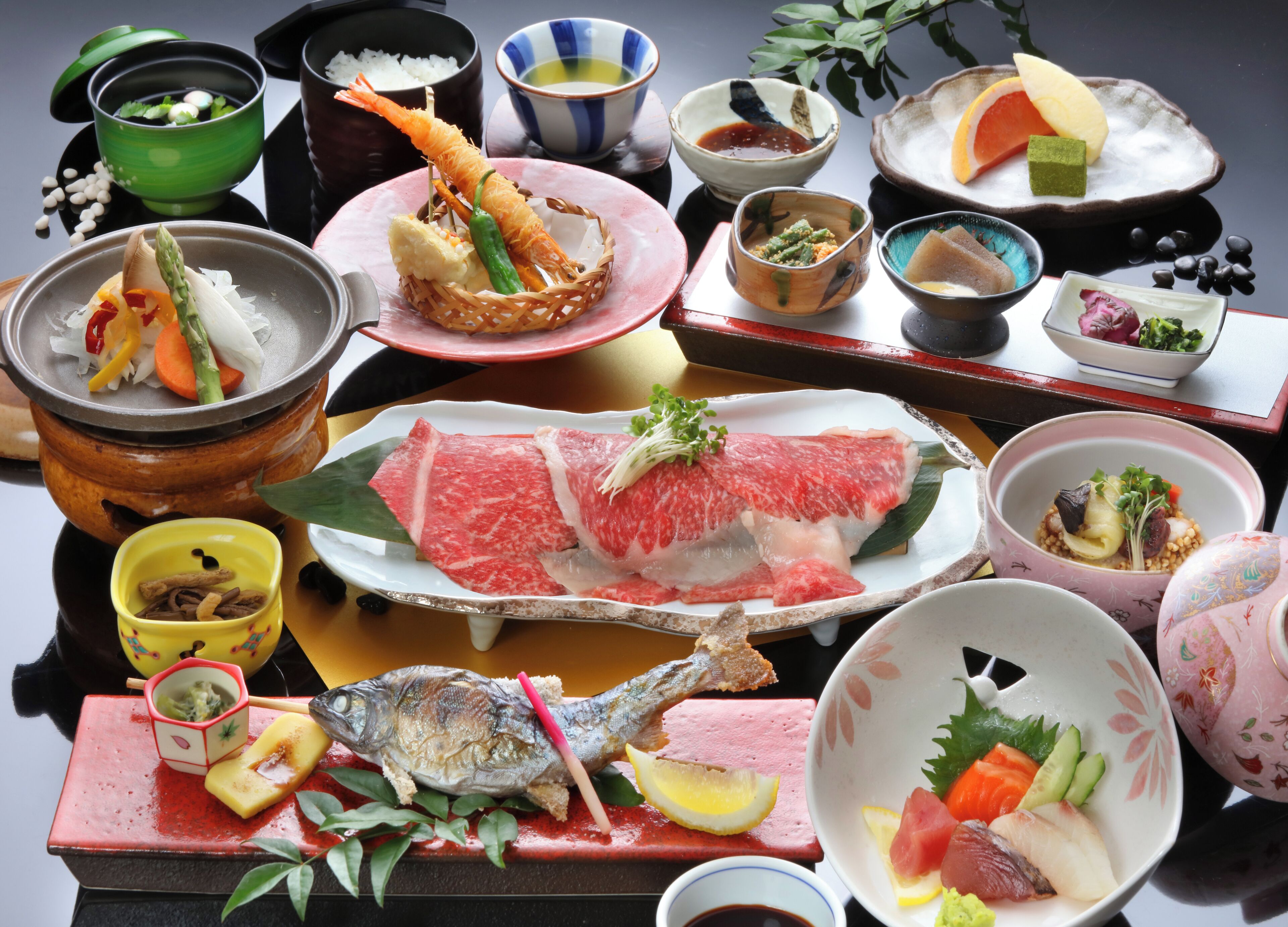 Variedad de platos que incluyen sashimi, pescado y verduras, dispuestos sobre una mesa con varios cuencos y fuentes.