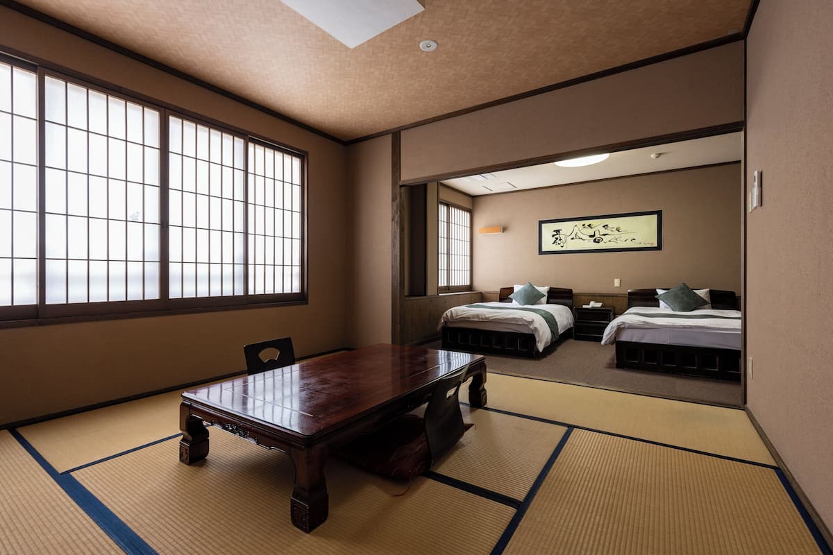 Une pièce de style japonais traditionnel, avec un sol recouvert de tatamis, une table en bois et deux lits équipés d’oreillers.