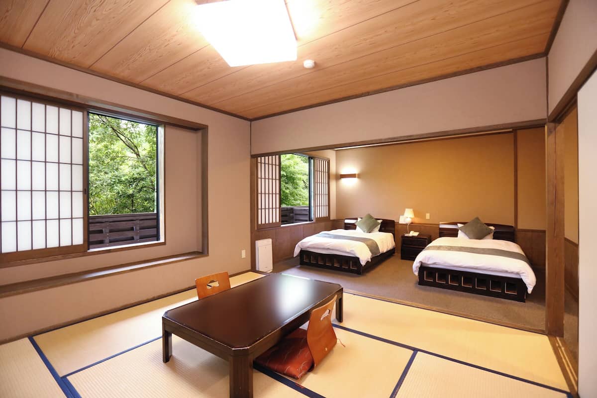 Une pièce de style japonais traditionnel, avec un sol recouvert de tatamis, une table en bois, deux lits équipés de futons et des portes coulissantes.