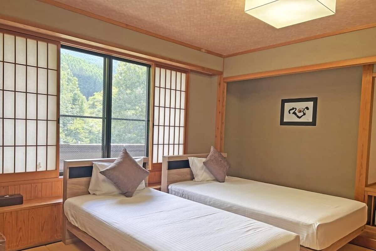 Une pièce de style japonais traditionnel, avec deux lits, un sol recouvert de tatamis, des paravents shoji et un tableau encadré au mur.