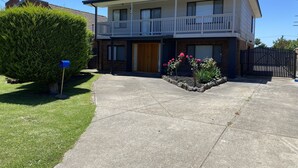 A two-story residential building with a balcony, a front door, and a small garden with pink flowers. - Dromana Charmer - Large family home, 8 min easy walk to the beach. (Dromana)